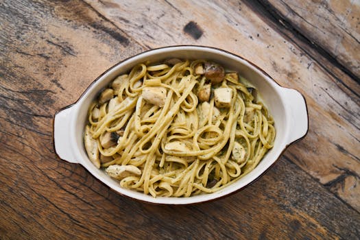 Tasty Italian pesto pasta with chicken served in a white dish on a wooden table.